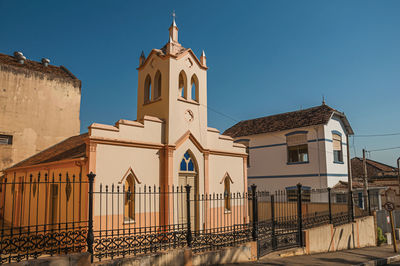 Facade of small church and belfry behind iron fence, in a sunny day at são manuel, brazil.