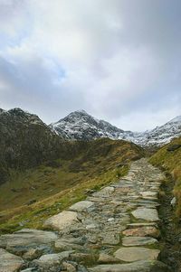 Stone footpath leading towards mountains against cloudy sky