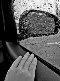 Cropped hand by wet car window during rainy season