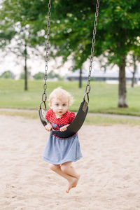 Full length portrait of cute girl leaning on swing over sand