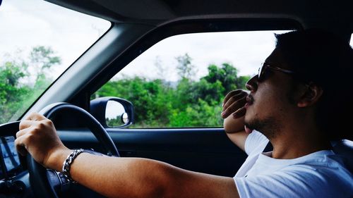 Side view of young man wearing sunglasses while sitting in car