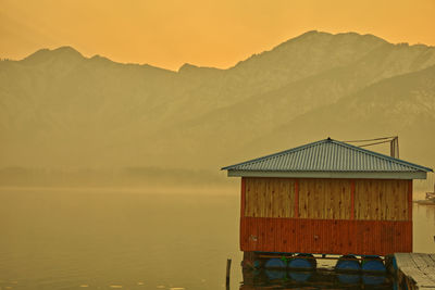 House by lake against sky during sunset