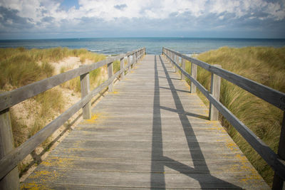 Boardwalk leading towards sea against sky