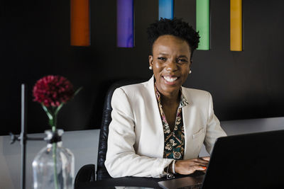 Happy young businesswoman with laptop sitting at desk in office