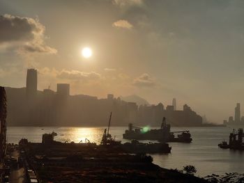 Silhouette city by sea against sky during sunset