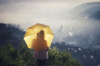 Rear view of woman with umbrella standing against land