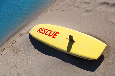 High angle view of yellow surfboard with rescue text at beach