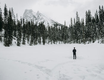 Lone man in suit stands alone on snow covered lake with mountains