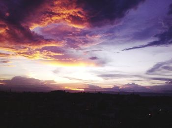 Silhouette city against dramatic sky during sunset