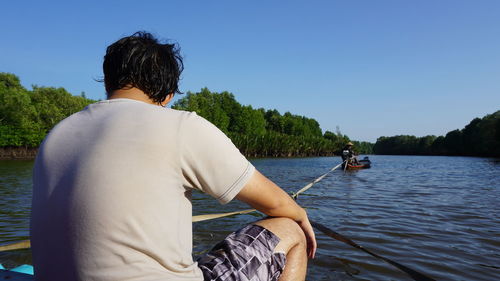 Rear view of man in boat sailing on river against clear sky