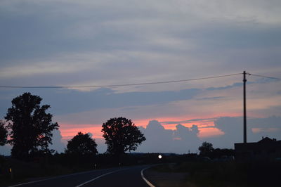 Road by silhouette trees against sky during sunset