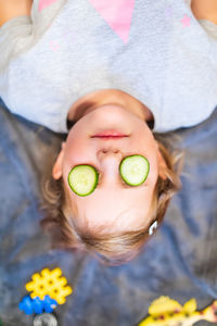 High angle view of girl lying upside down with cucumber slices on eyes in spa