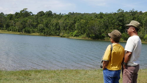 Rear view of friends standing by lake against trees