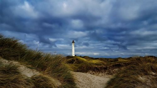Lighthouse on grassy field against cloudy sky