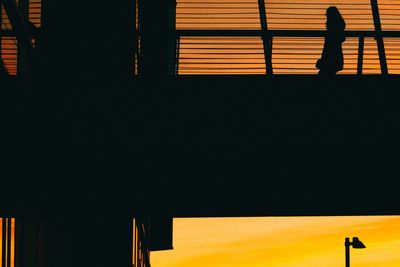 Silhouette people standing by building against orange sky