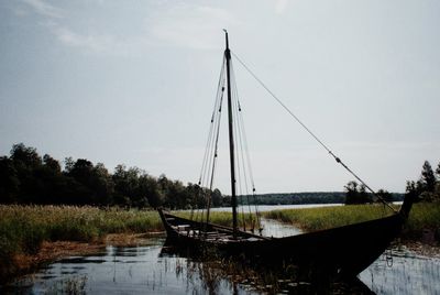 Boat moored on grass by trees against sky