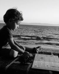 Boy sitting on beach against sky