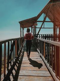 Rear view of woman with backpack walking on footpath against clear sky