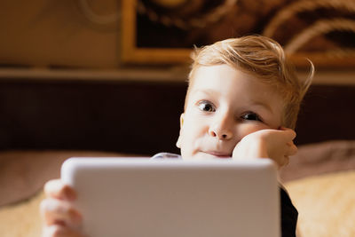 Small boy using digital tablet at home and looking at camera.