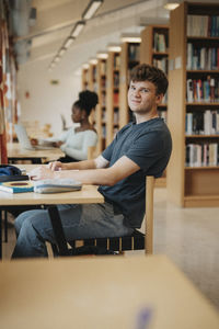 Portrait of smiling student sitting at table while studying in library