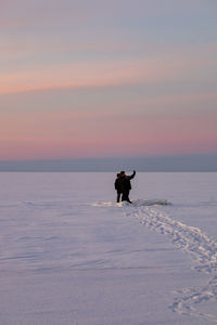 Side view of woman walking on snow covered beach against sky during sunset
