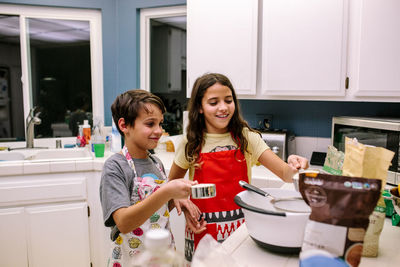 Brother and sister smile while baking in the kitchen at night