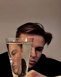 Young man reflecting in drinking glass