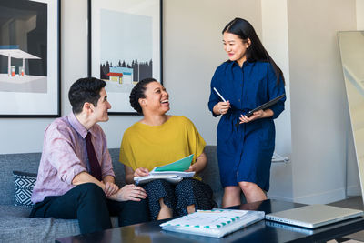 Happy male and female colleagues looking at businesswoman with graphics tablet in office