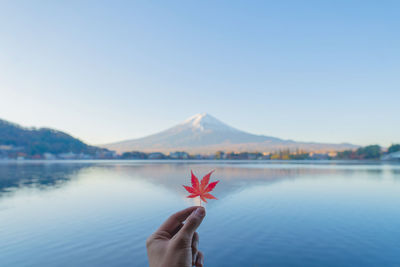 Person holding umbrella by lake against sky