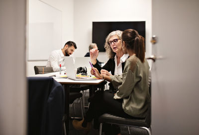 Senior businesswoman discussing with female colleague at conference table in board room