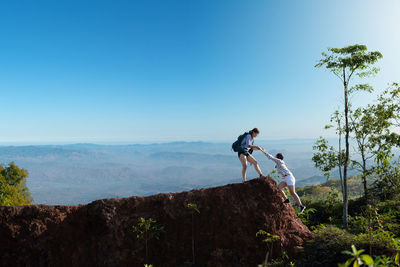 Side view of man on rock against sky