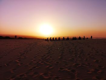 Silhouette people sitting at beach against sky during sunset