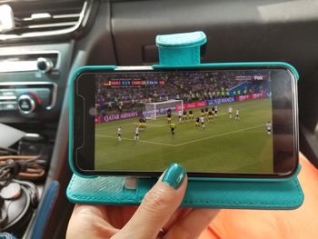 Close-up of person hand watching tv on mobile phone in car