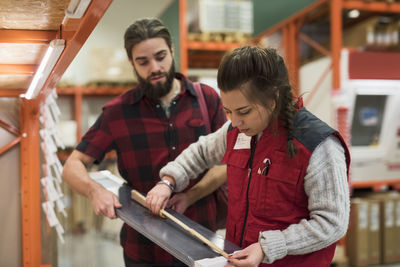 Saleswoman measuring metal plank with folding ruler while standing by customer in hardware store