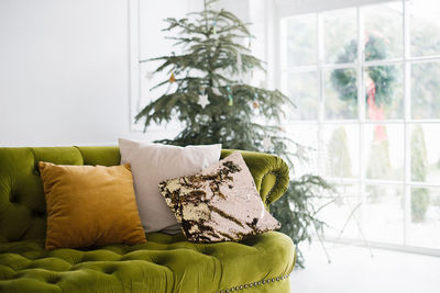 Christmas comfort. christmas tree, pillows on the green sofa in the bright living room