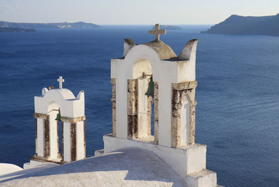 Cross on sea by building against sky