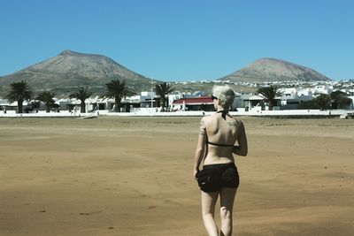 Rear view of woman on beach against clear blue sky