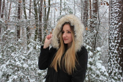 Thoughtful young woman in warm clothing standing at forest during winter