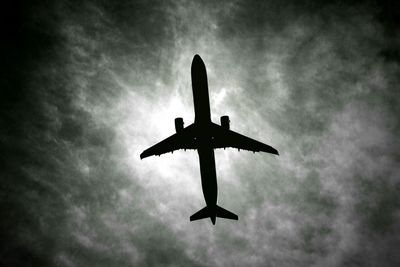 Low angle view of bird flying against cloudy sky