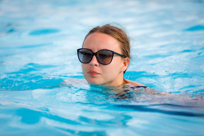 A young, beautiful girl in sunglasses swims in the pool. high quality photo