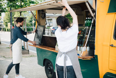 Male owner adjusting board on concession stand while female coworker opening shade of food truck