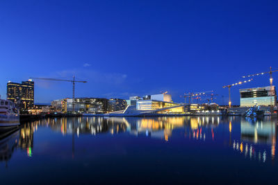 Illuminated city by river against clear blue sky at night