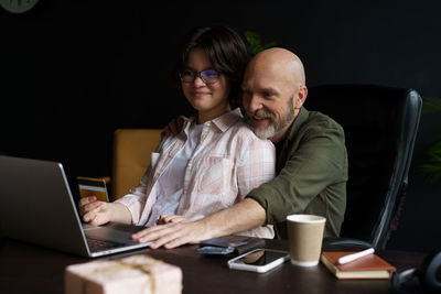 Friends using laptop while sitting on chair at home