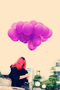 Rear view of woman with pink balloons against sky