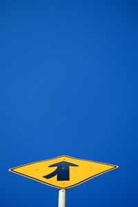 Low angle view of road sign against clear blue sky