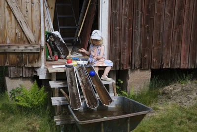 Boy sitting on wooden chair against plants