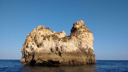 Rock formation in sea against clear blue sky