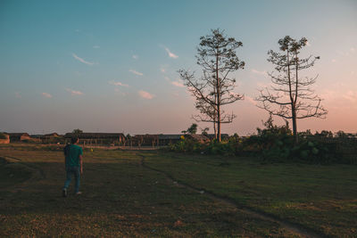 Rear view of man standing on field against sky during sunset