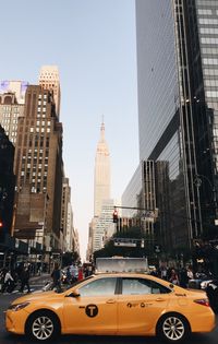 Yellow taxi against empire state building on road in city