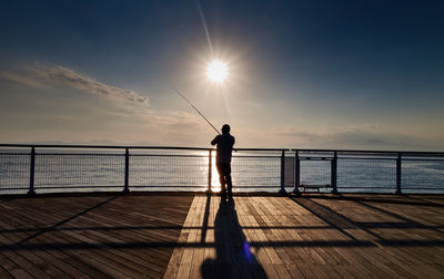 Silhouette man fishing in sea against sky during sunset